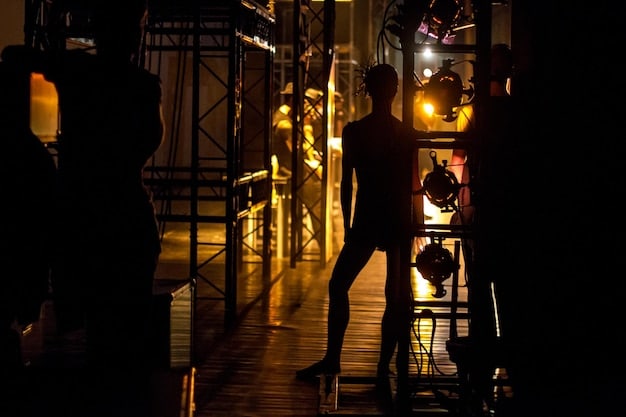 An artist setting up equipment on a concert stage, preparing for a live performance. The venue is a mid-sized theater with ambient lighting and a focused look.