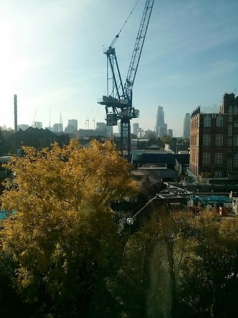 A construction site showing progress of building Olympic facilities, with cranes and workers operating, with a city skyline in the background.