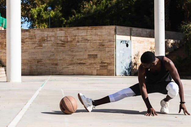 A basketball player performing a dynamic leg swing exercise on the court, stretching his hamstring and glutes during a pre-game warm-up.