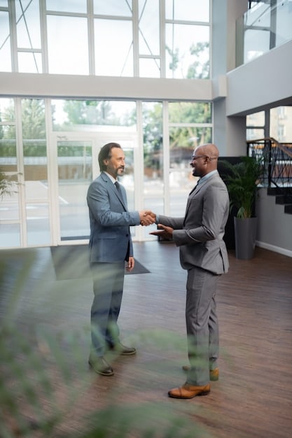 Two business people shaking hands with a government official in a modern office setting, with a subtle background featuring flags or government building imagery, symbolizing successful partnership and funding approval.